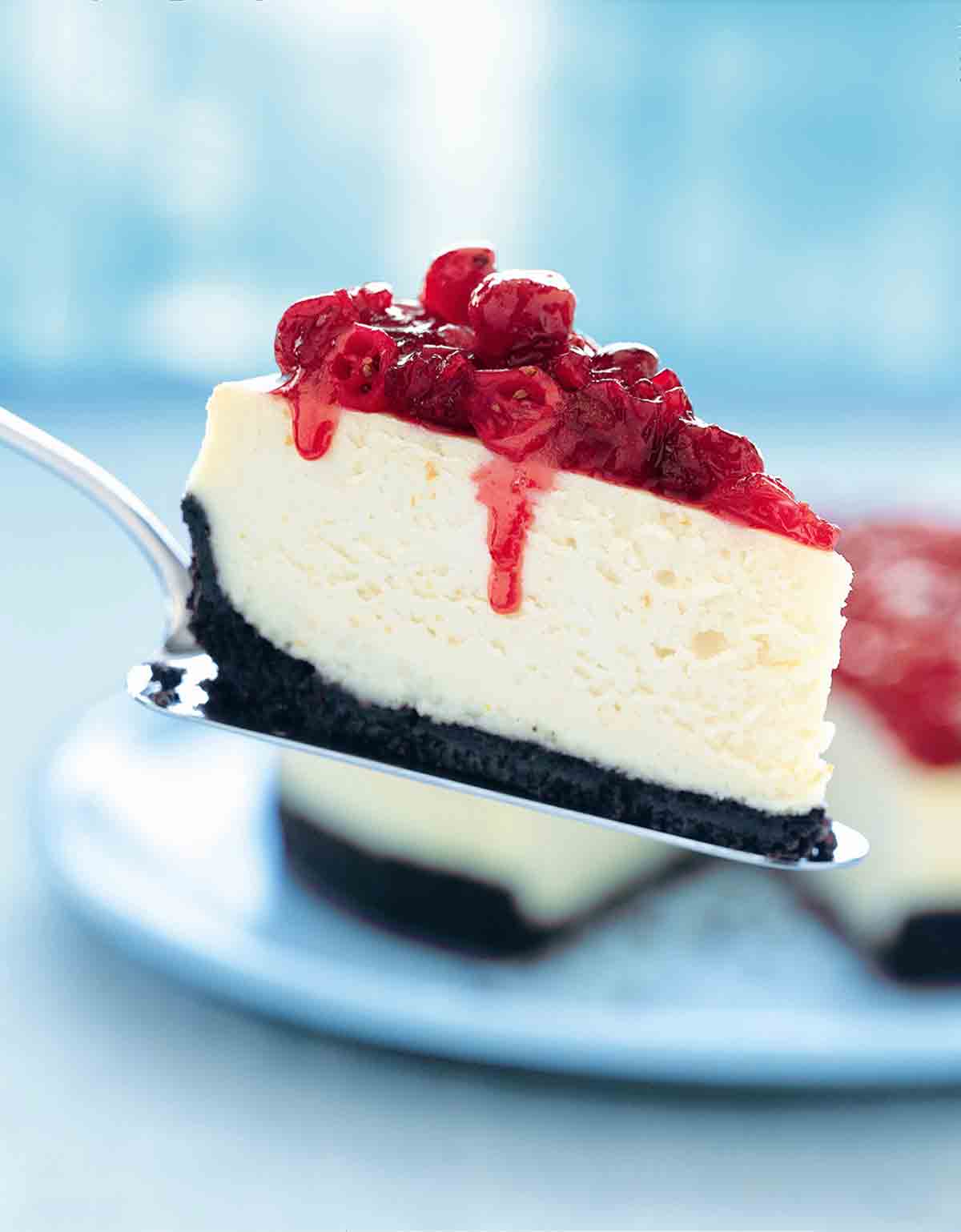 A slice of cheesecake topped with cranberries on a silver cake lifter.