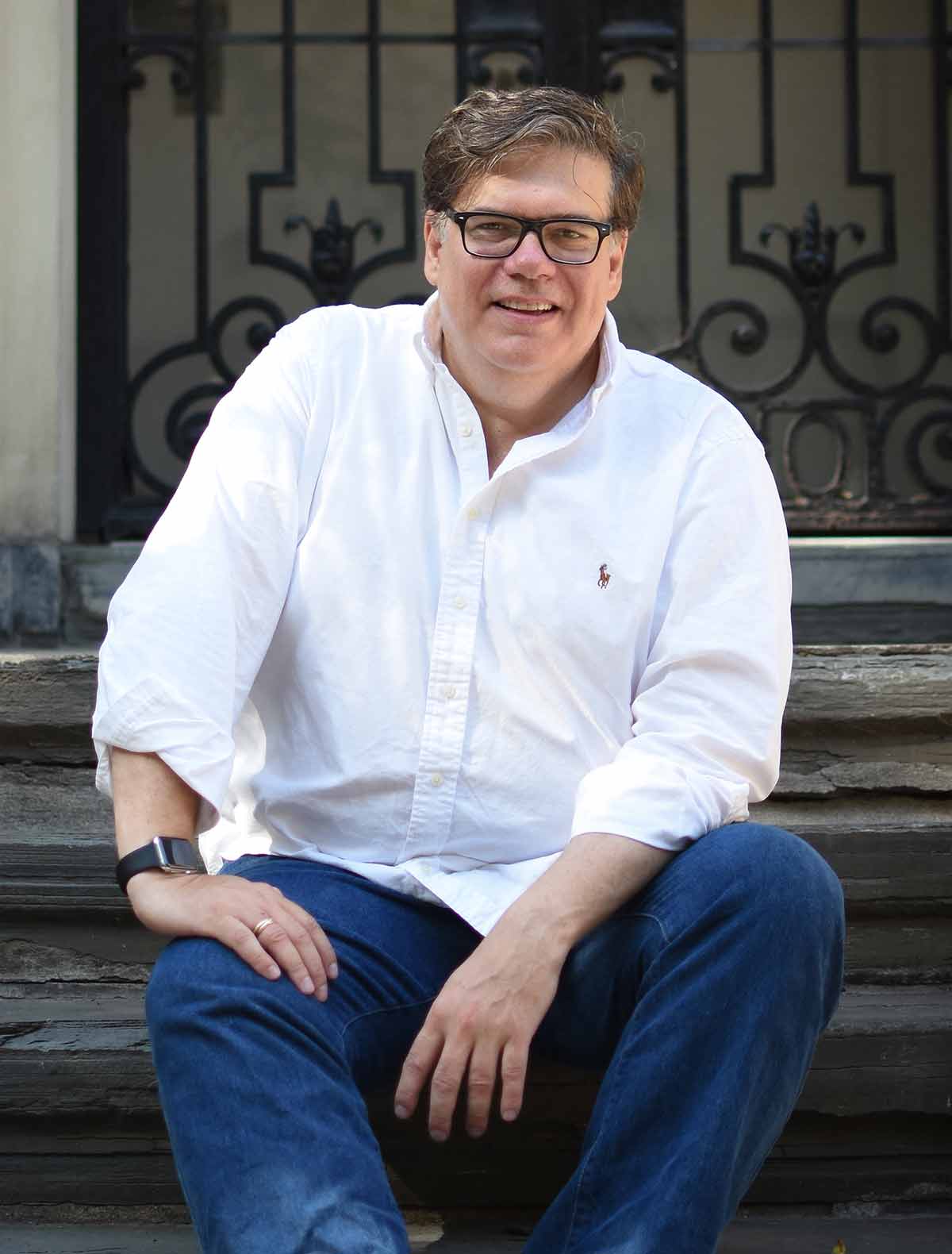 A man in a white shirt sitting on the stoop of a brownstone.