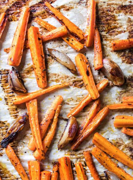 A baking sheet lined with parchment and covered with easy roasted carrots and onions with burnt edges.