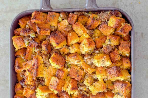 Casserole dish of cubes of homemade cornbread sausage dressing, with pork sausage, onion, celery, and spices.
