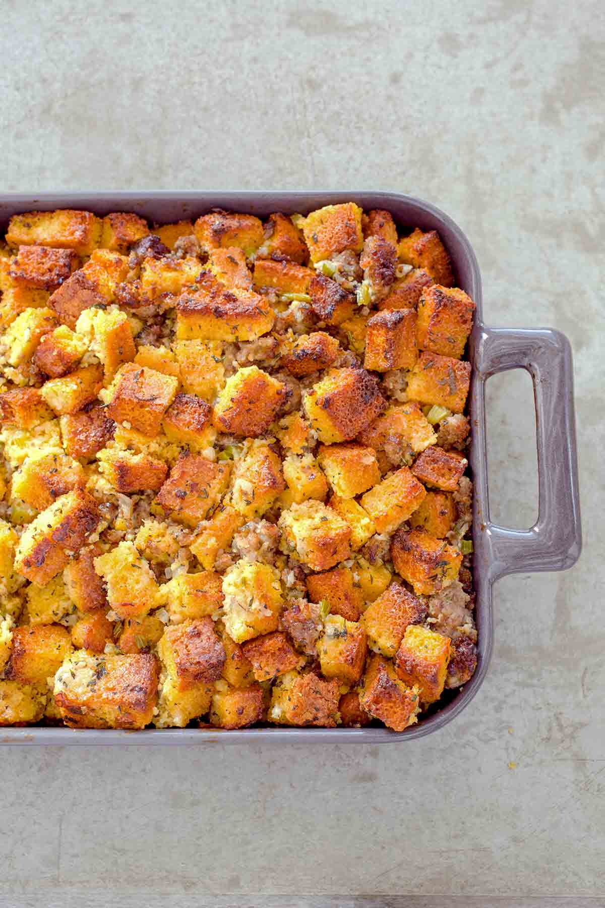 Casserole dish of cubes of homemade cornbread sausage dressing, with pork sausage, onion, celery, and spices.