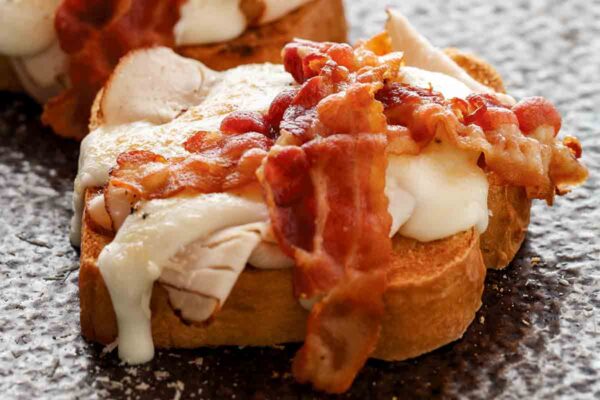 Two open-faced sandwiches topped with turkey, white sauce, and two slices of bacon.