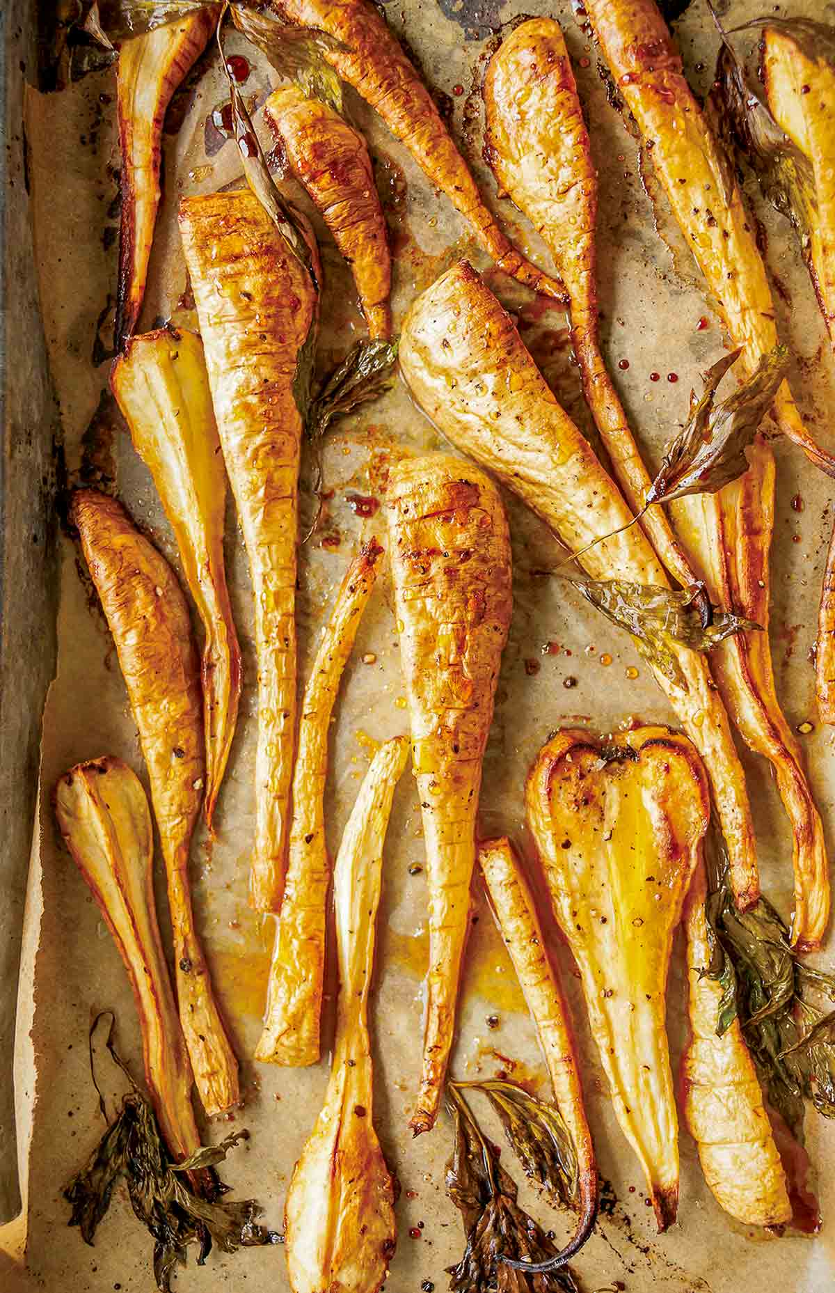 Sheet pan lined with parchment and sliced maple roasted parsnips.