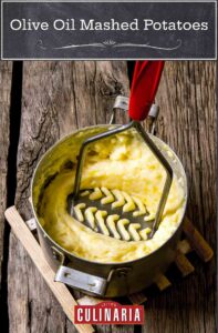 A potato masher pressing down in a pot of olive oil mashed potatoes.