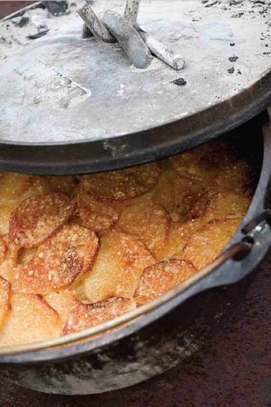 A partially covered Dutch oven filled with cooked Parmesan potato gratin.