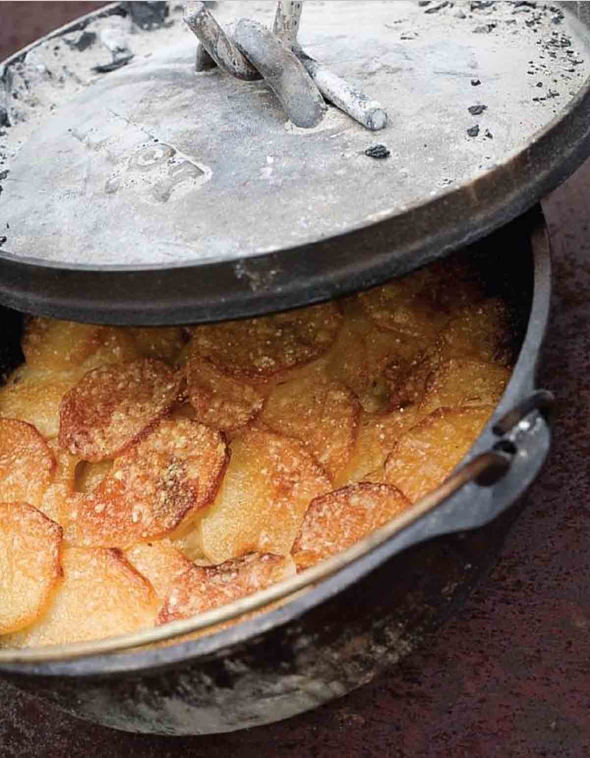 En delvis täckt holländsk ugn fylld med kokt parmesan potatisgratäng.