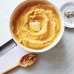A big pot of pumpkin mashed potatoes with a pat of butter on top, wooden spoon on the side.