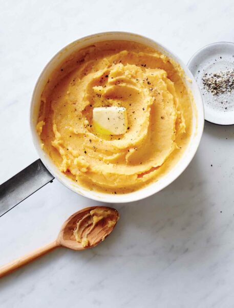A big pot of pumpkin mashed potatoes with a pat of butter on top, wooden spoon on the side.