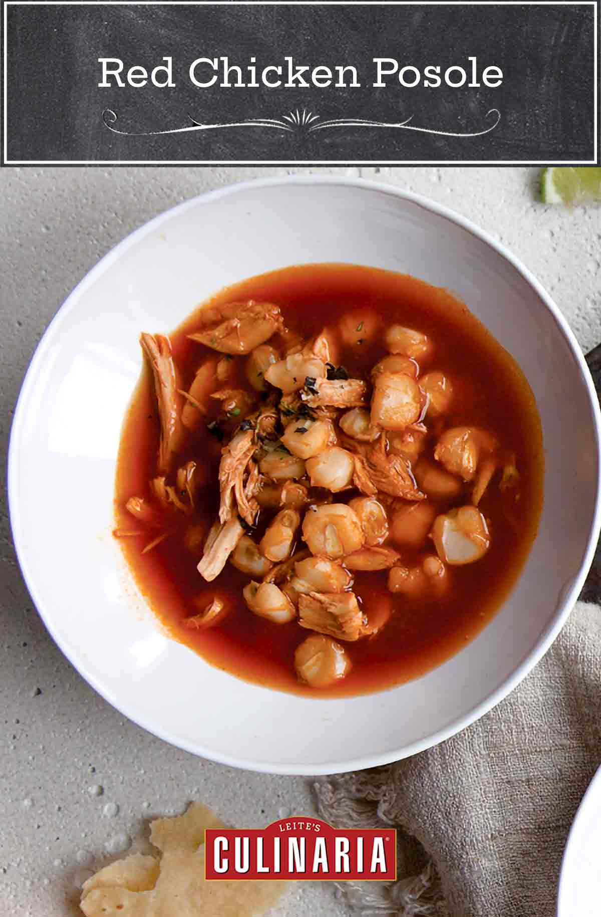Two white bowls filled with red posole with pieces of tortilla and lime wedges on the side.