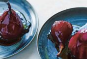 Two blue plates with red wine poached pears and a drizzle of sauce over them.
