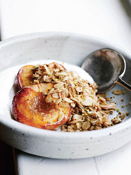A white bowl of roast peaches topped with an easy granola of oats and almonds, Greek yogurt underneath.
