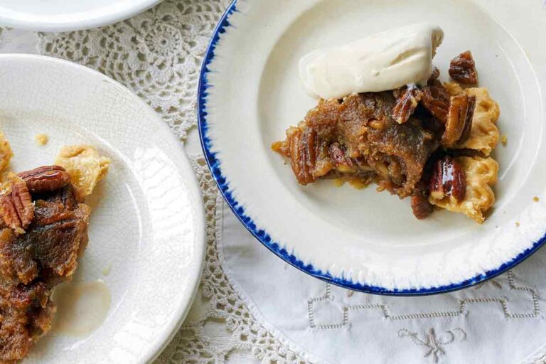 Four plates of rum pecan pie in a flaky crust, topped with whole pecans and vanilla ice cream.