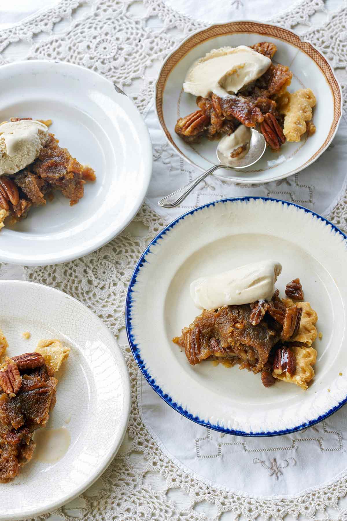 Four plates of rum pecan pie in a flaky crust, topped with whole pecans and vanilla ice cream.