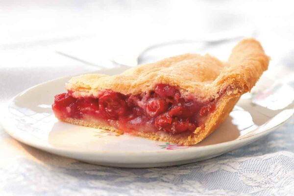 A slice of sour cherry pie on a white plate.