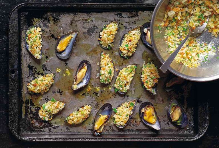 Several opened mussels on a baking sheet, some filled with stuffing and a bowl of extra stuffing on the side.