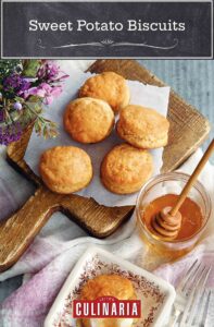 A cutting board with five sweet potato biscuits on it and a square plate square with a split biscuits spread with butter and honey.