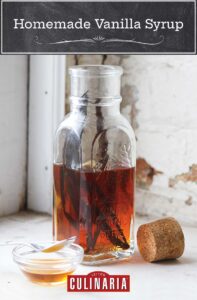 A bottle half-filled with vanilla syrup and a couple vanilla beans inside. A cork rests beside the bottle.