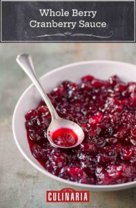A white bowl filled with whole berry cranberry sauce with a silver spoon resting in it.