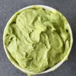 A container of green avocado sorbet ona slate surface.