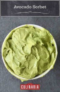 A container of green avocado sorbet ona slate surface.