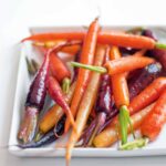 White plate filled with orange, purple, and yellow candied carrots.