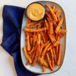 An oval platter filled with carrot fries and a small bowl of chipotle dipping sauce.