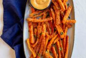 An oval platter filled with carrot fries and a small bowl of chipotle dipping sauce.