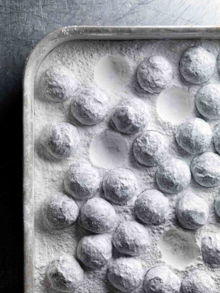 A rimmed sheet pan filled with truffles coated in confectioners' sugar.