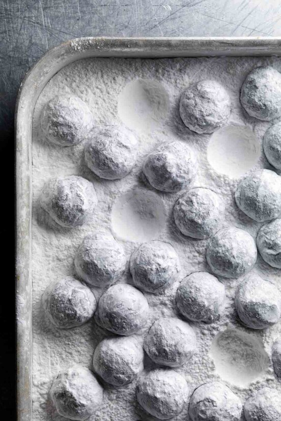 A rimmed sheet pan filled with truffles coated in confectioners' sugar.