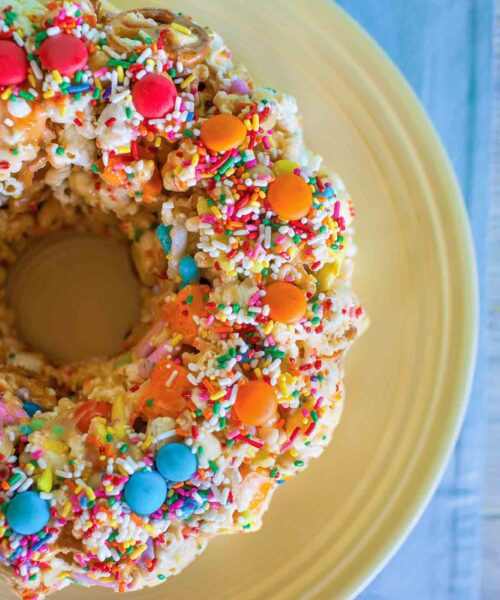 A popcorn cake with sprinkles M&Ms on top on a yellow plate.