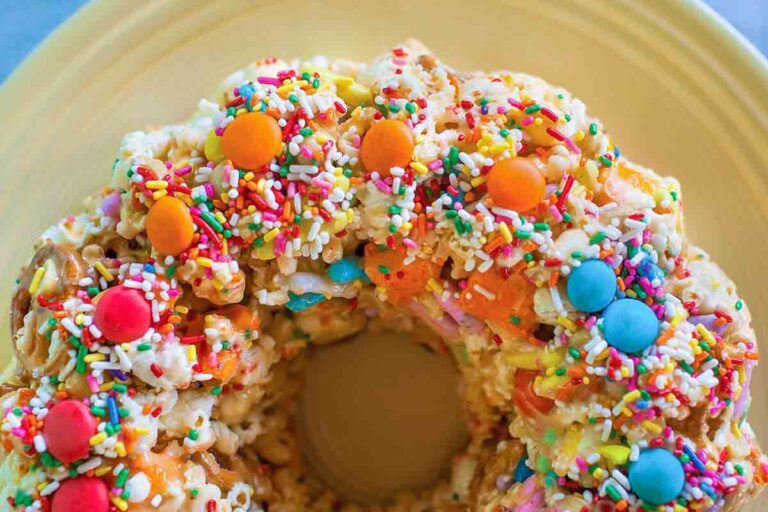A popcorn cake with sprinkles M&Ms on top on a yellow plate.