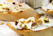 Toasted rounds of baguette topped with goat cheese and chopped pistachios with a dish of honey in the background.