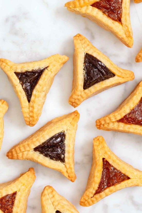 Ten hamantaschen -- jam filled, triangle-shaped pastries -- on a white background.