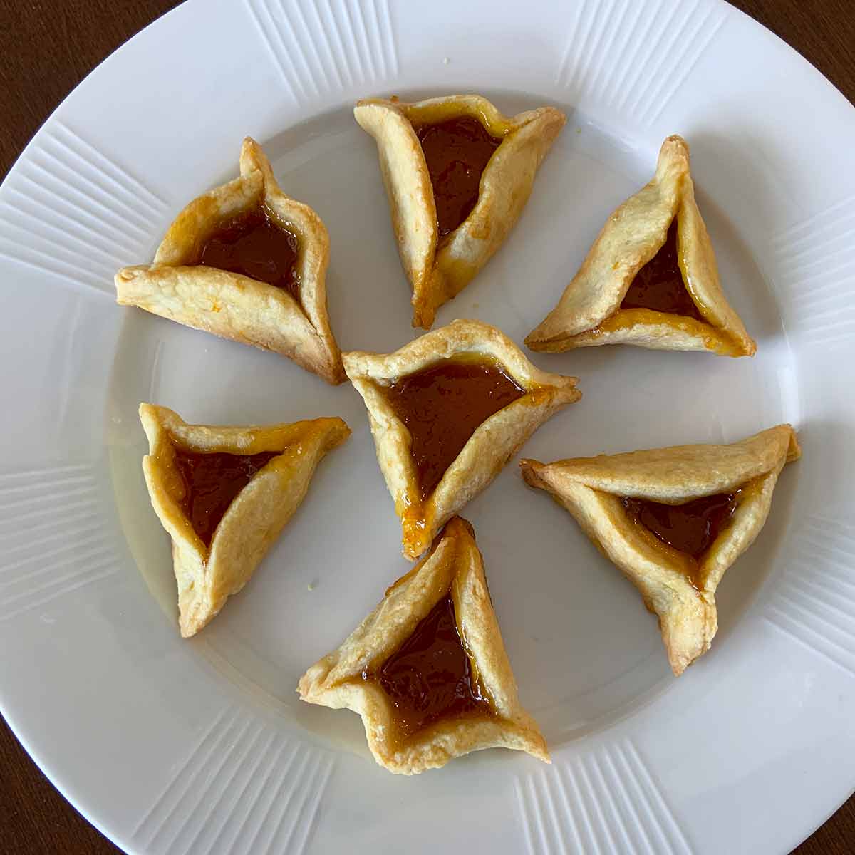 Seven hamantaschen -- jam filled, triangle-shaped pastries -- on a white plate.