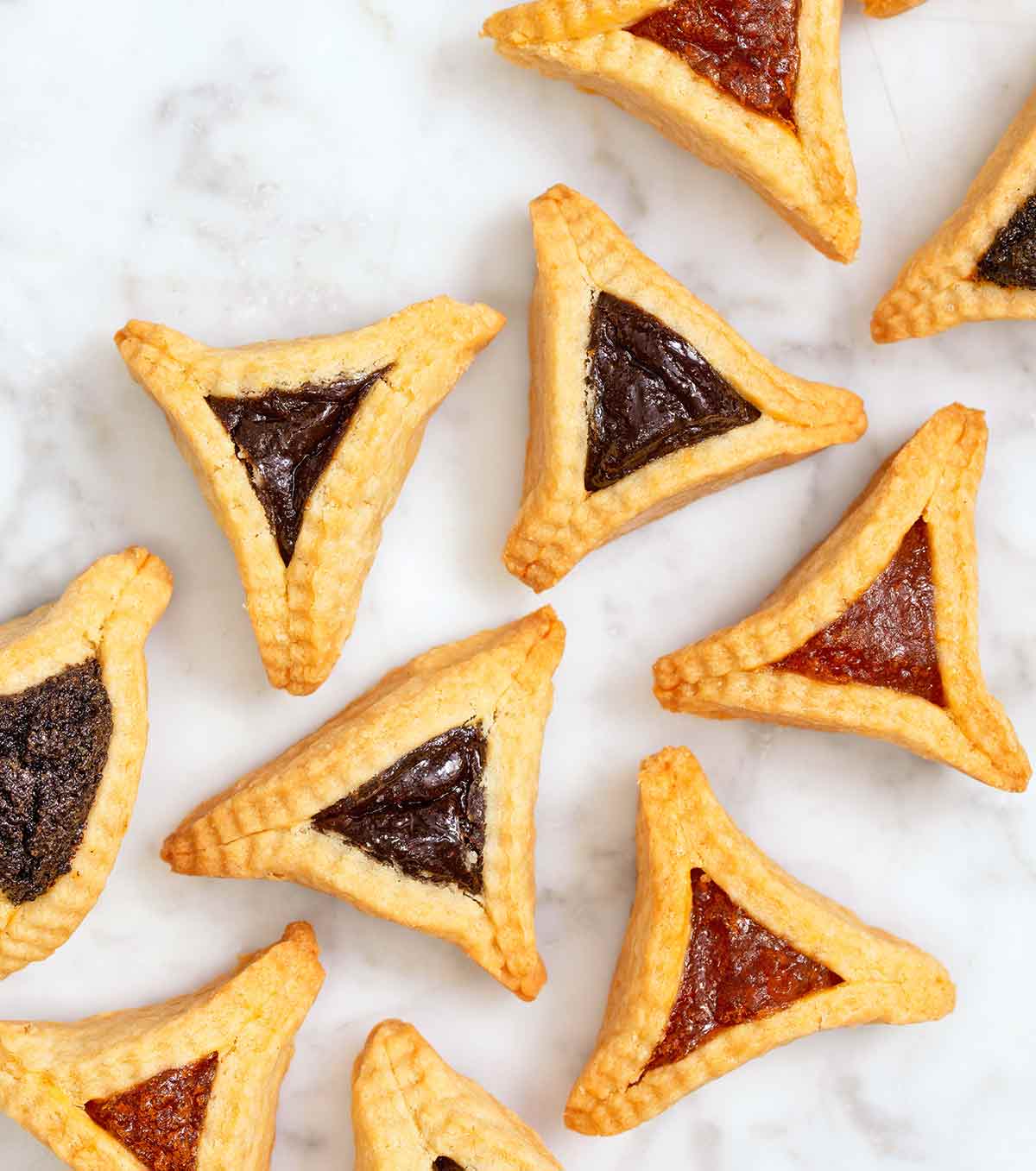 Ten hamantaschen -- jam filled, triangle-shaped pastries -- on a white background.