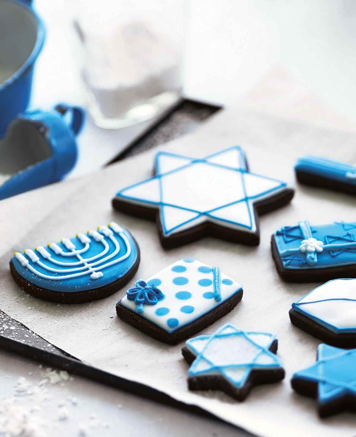 A selection of frosted cookies decorated for Hanukkah, on a parchment-lined cookie sheet.