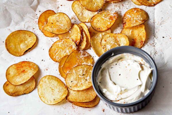 Homemade potato chips on a crumpled piece of parchment paper and a bowl of sour cream.