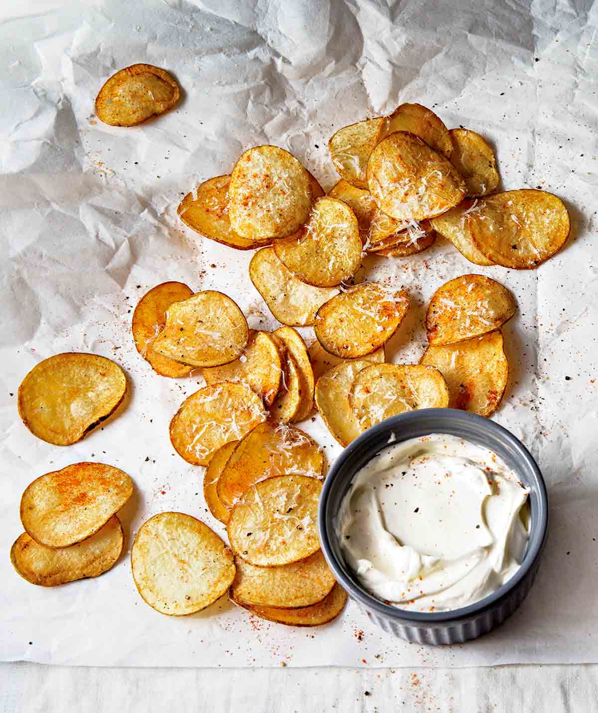 Homemade potato chips on a crumpled piece of parchment paper and a bowl of sour cream.