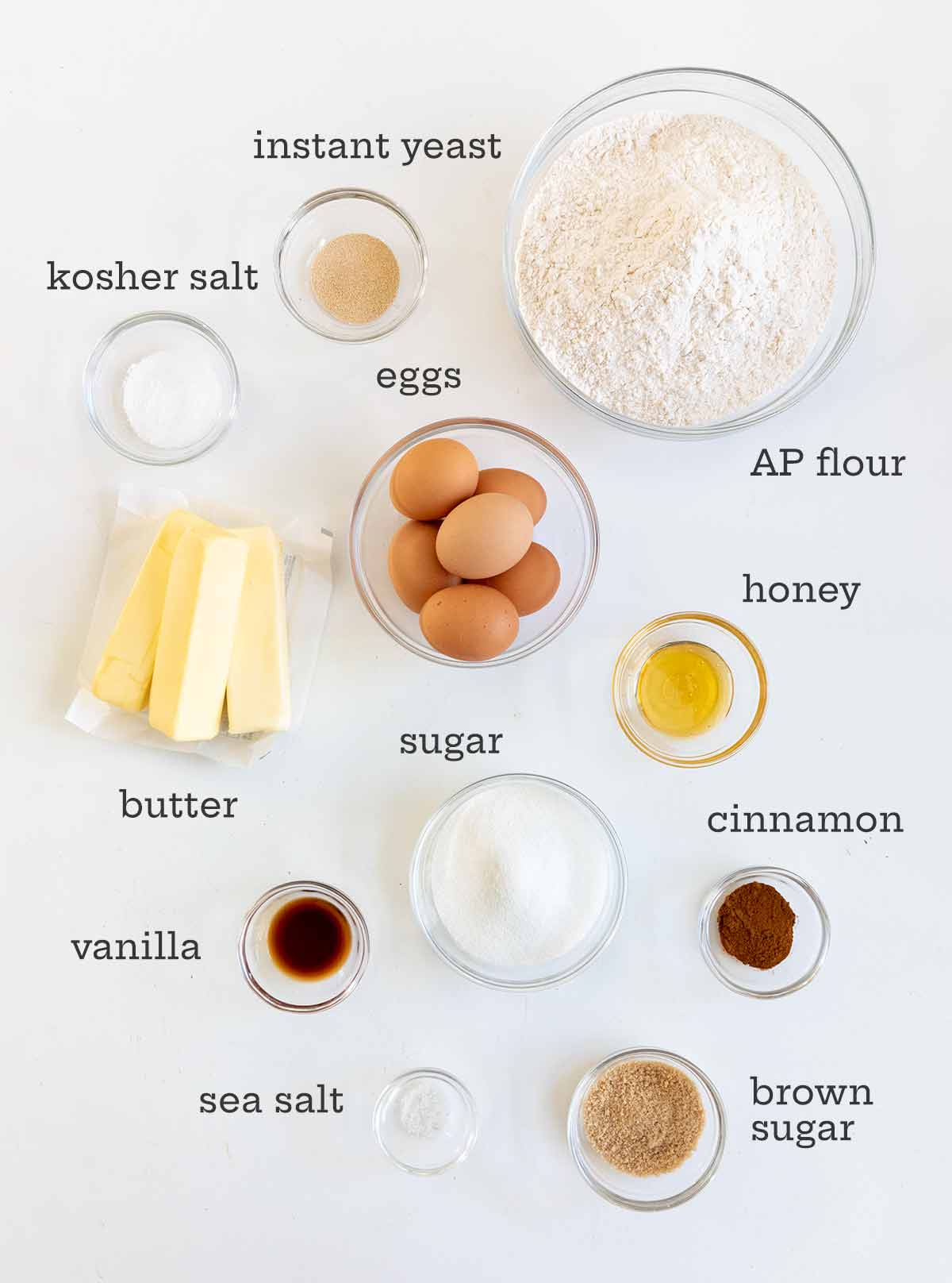 Monkey bread ingredients: bowls of flour, eggs, yeast, sugar, butter, brown sugar, vanilla, cinnamon.