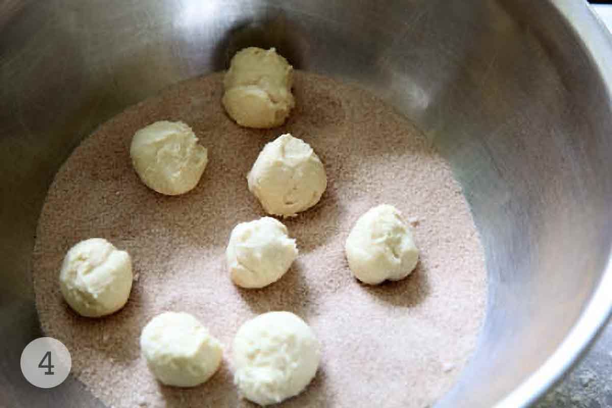 Balls of monkey bread dough in a bowl of cinnamon sugar.