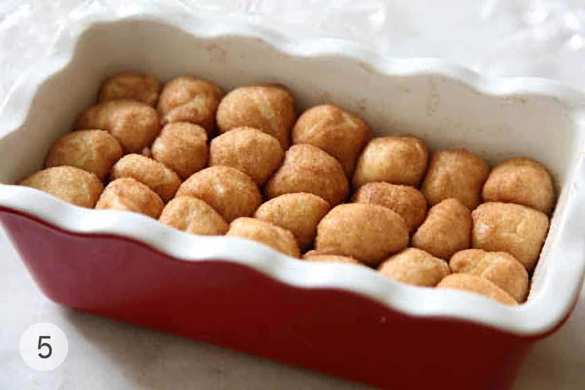 Rows of unbaked monkey bread balls in a red rectangular baking dish.