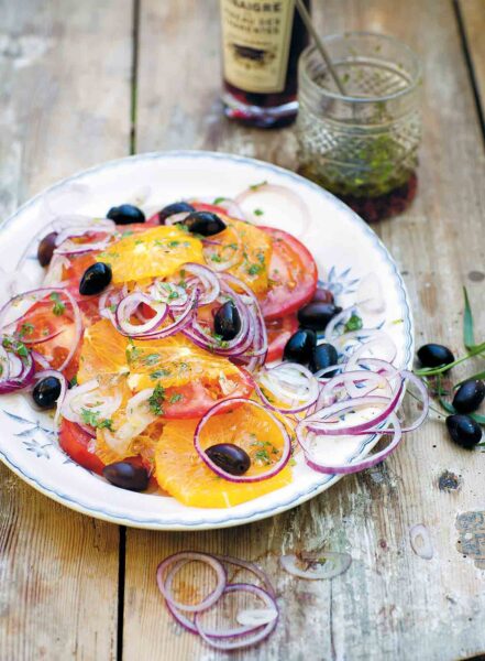 A patterned plate topped with a Moroccan salad made with sliced oranges and tomatoes, black olives, and sliced red onion.