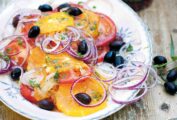 A patterned plate topped with a Moroccan salad made with sliced oranges and tomatoes, black olives, and sliced red onion.