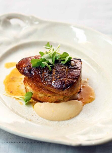 A plate with a large piece of seared foie gras topped with watercress and apple puree on the side.