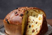 A panettone studded with dried fruit on a silver platter with a couple of wedges cut from it.