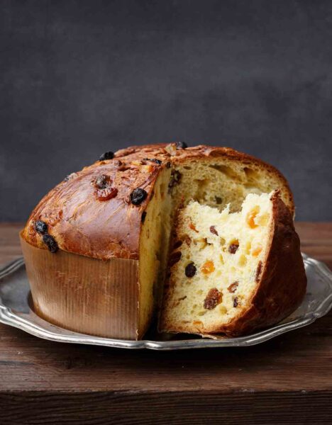 A panettone studded with dried fruit on a silver platter with a couple of wedges cut from it.