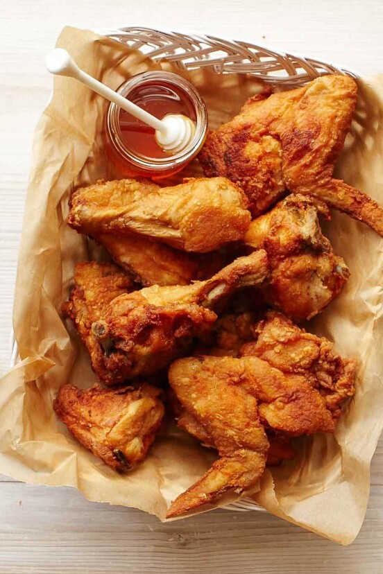 A basket of fried chicken with a jar of honey on the side.