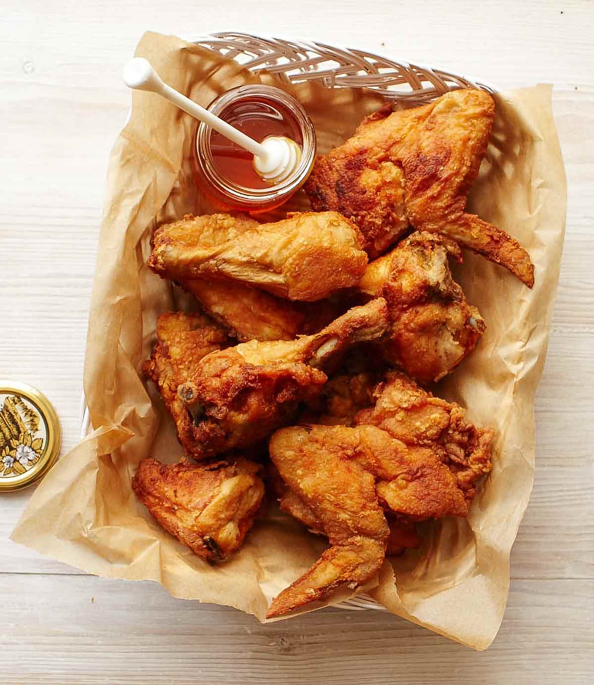 A basket of fried chicken with a jar of honey on the side.