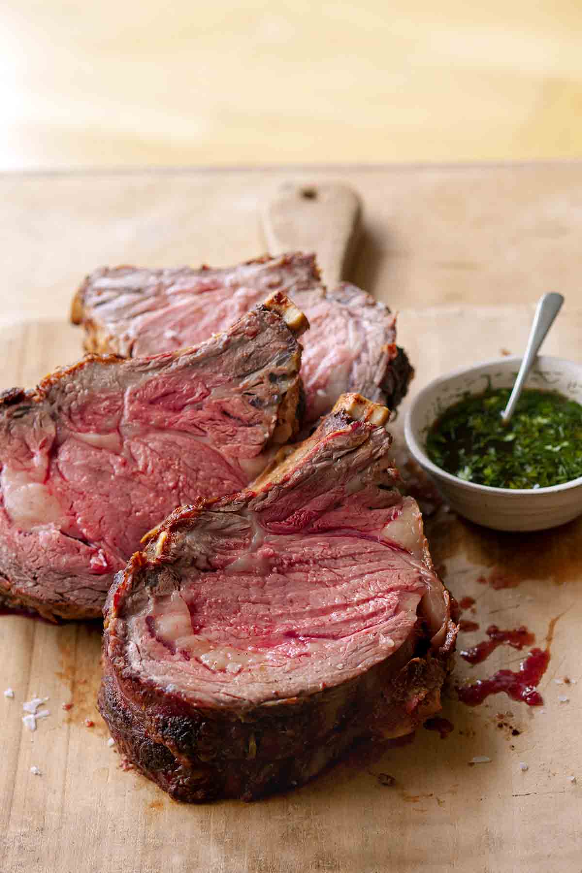 Three slice of medium rare standing rib roast au jus on a cutting board.