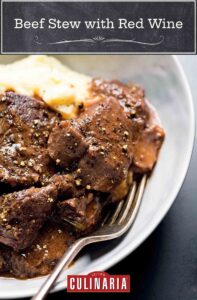 Pieces of beef stew with red wine and mashed potatoes in a white bowl with a fork nestled inside.